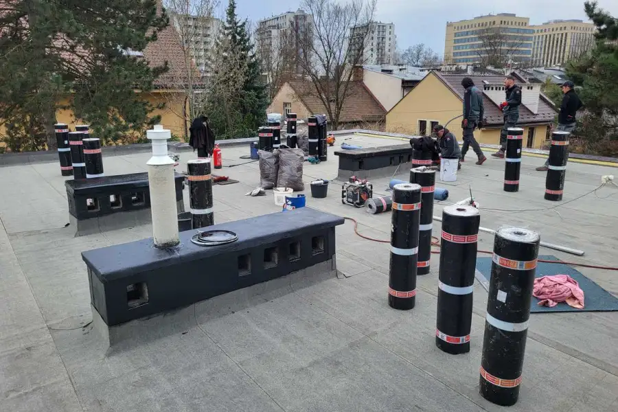Toit-terrasse d'un immeuble urbain en pleine réfection d'étanchéité : une vingtaine de rouleaux de membrane bitumineuse dressés à la verticale sur la dalle.