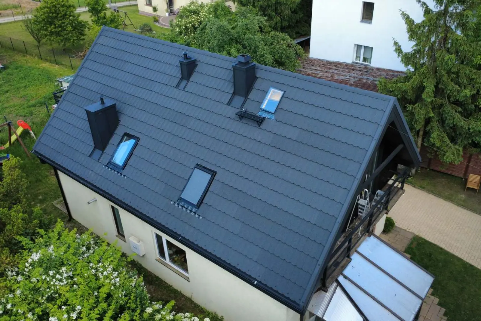 Vue drone d'une maison individuelle dont la toiture à deux pans vient d'être refaite en tuiles métalliques anthracite à granulés : deux souches de cheminée habillées de métal noir.